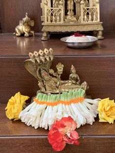 an ornate statue sitting on top of a wooden table next to yellow and red flowers