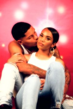 a man and woman sitting next to each other in front of a red wall with lights