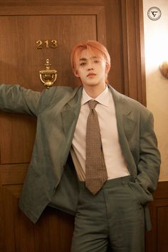 a man with red hair wearing a suit and tie leaning against a wooden door holding his hands on his hips