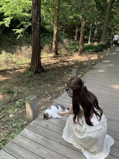 a woman kneeling down petting a cat on top of a wooden platform in the woods