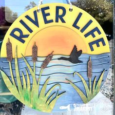 a sign that says river life on the side of a glass window with water and grass