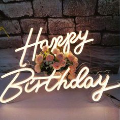 there is a birthday sign with flowers on it and the words happy birthday are lit up