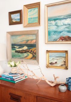 there are many pictures on the wall above the dresser in this living room, including paintings and seashells