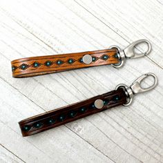 two wooden key chains with metal clasps on top of a white wood floor next to each other