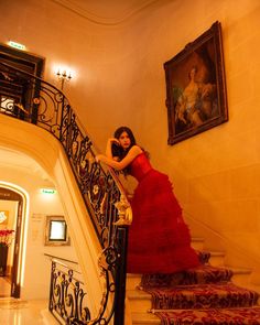 a woman in a red dress is standing on the stair case next to a painting