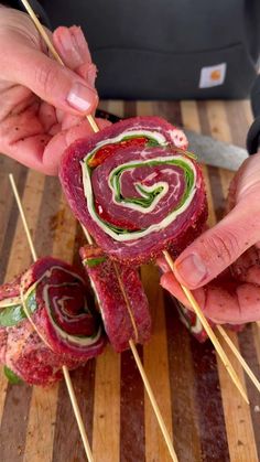 two hands are holding skewers with meat and veggies wrapped in strips