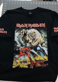 a black iron maiden t - shirt sitting on top of a cutting board next to scissors