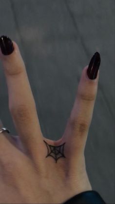 a woman's hand with a black spider web tattoo on her thumb and finger