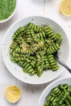 two bowls filled with pesto pasta next to lemon wedges and sauce on the side