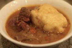 a white bowl filled with meat and vegetable soup on top of a counter next to a spoon