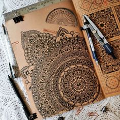 an open notebook with intricate designs on it and some crochet doily next to scissors