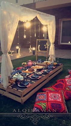 a table set up with food and lights on the grass in front of a building