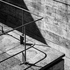 a black and white photo of a metal hand rail on concrete steps near a wall