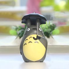 a black and yellow totoro with an umbrella on it's head sitting in front of a potted plant