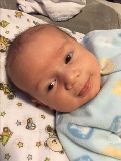 a close up of a baby laying in a bed with a blanket on it's back