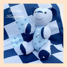 a blue and white teddy bear sitting on top of a checkerboard blanket with words above it