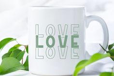 a white coffee mug sitting on top of a table next to some green leafy plants