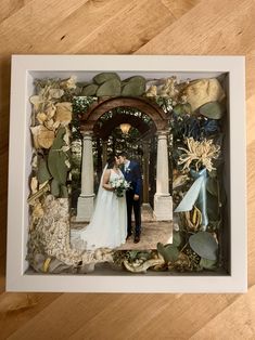 a couple standing in front of an arch surrounded by leaves and flowers on a wooden floor