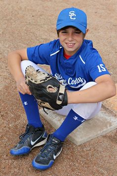 a young baseball player sitting on the ground with his mitt in front of him