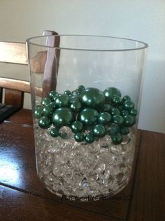 a glass filled with green balls on top of a wooden table