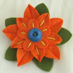 an orange flower with green leaves and a blue button in the center on a white surface