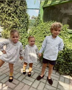 three young children are walking down the sidewalk in their dresses and socks, one is holding hands with the other