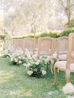 rows of chairs lined up in the grass with white flowers on each chair and greenery behind them