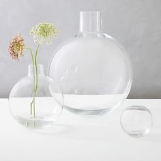 two clear vases with flowers in them on a white table top next to each other