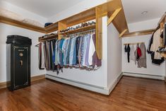 an organized closet with clothes hanging on wooden shelves and a black trash can in the corner