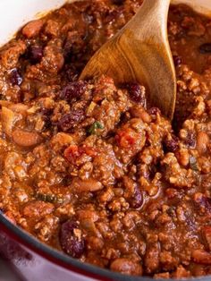 a wooden spoon in a pot full of chili and beans with meat on the side