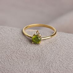 a yellow gold ring with a peridolite stone in the center on a gray surface