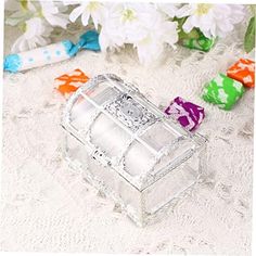 a glass box with candy in it sitting on a table next to white flowers and colorful candies