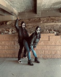 two people dressed up in skeleton makeup and black clothing, one holding his hand up to the ceiling