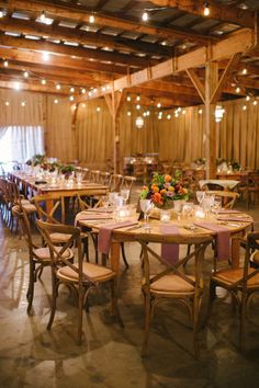 the tables and chairs are set up for a wedding reception in an old barn with lights hanging from the ceiling