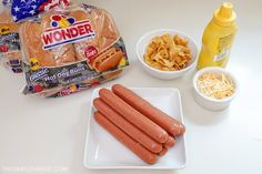 hotdogs, chips, and mustard on a white table with a bag of wonder