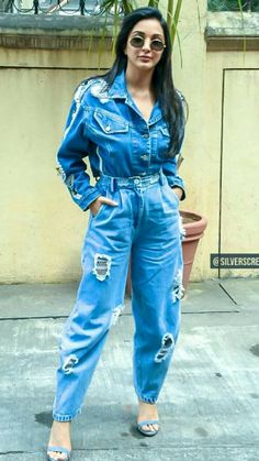 a woman standing in front of a potted plant wearing blue denim overalls and sunglasses