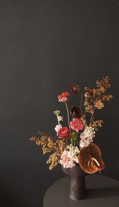 a vase filled with lots of different flowers on top of a gray table next to a black wall