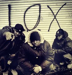 three young men sitting next to each other in front of a wall with graffiti on it