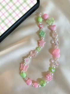 ♡ Pastel Pink and Green Phone Charm/Strap ♡ Approximately 7 inches in length from top of cord to bottom of beads ♡Made with: * white waxed cord * beige acrylic pearls * plastic and clay beads ♡ Beads and bead colors may vary but will look very similar to the phone charm pictured ♡ Please contact me if you have any questions or any bead color preferences Phone Charms Pastel, Pink And Green Phone Case, Pink And Green Accessories, Pastel Phone Charm, Phone Beads Strap Aesthetic, Pink Phone Charm Aesthetic, Kandi Phone Charm, Handmade Pink Plastic Necklace, Cute Spring Adjustable Beaded Necklaces