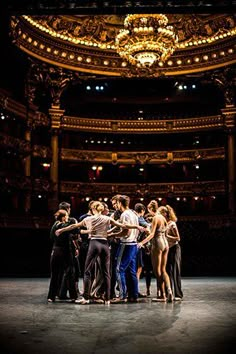 a group of people standing around each other in front of a stage with chandelier