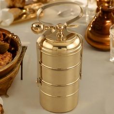 a gold canister sitting on top of a table next to other plates and glasses