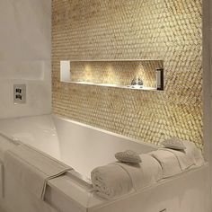 a white bath tub sitting next to a sink under a bathroom mirror with lights on it