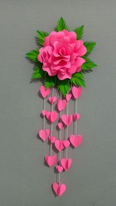 pink paper flowers are hanging from the side of a wall with hearts attached to them