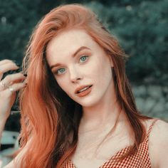 a woman with red hair and blue eyes is posing for a photo in front of some bushes