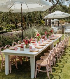 an outdoor table set up with pink and white chairs, plates and cups on it