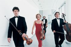 three people in tuxedos are walking down the hall with their violins behind them