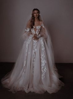 a woman in a wedding dress standing with her arms around her waist and wearing a veil