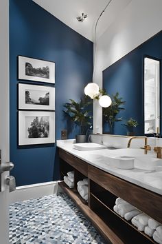 a bathroom with blue walls and pictures on the wall above the sinks, along with white towels