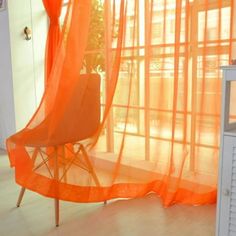 an orange chair sitting in front of a window with sheer curtains on the windowsill