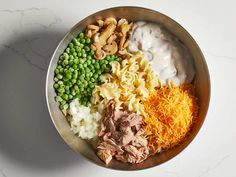 a bowl filled with pasta, peas, cheese and other toppings on top of a white table